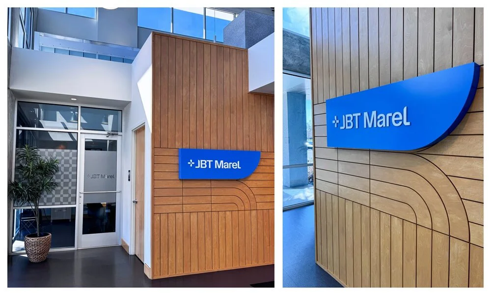 A collage of the blue JBT Marel logo and signage against a wood accented wall in the lobby. It also depicts the vinyl privacy door graphics.